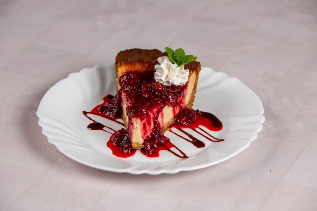 A close-up of a raspberry cheesecake slice with raspberry sauce and mint garnish.